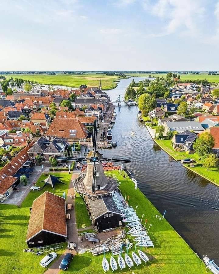 Aerial view of a Dutch village canal with a traditional windmill, boats, and red-roofed houses