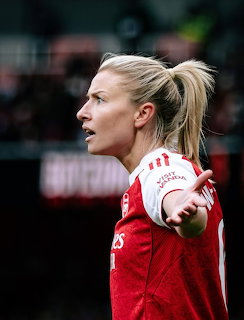 Profile of Leah Williamson in a red and white football jersey on the field