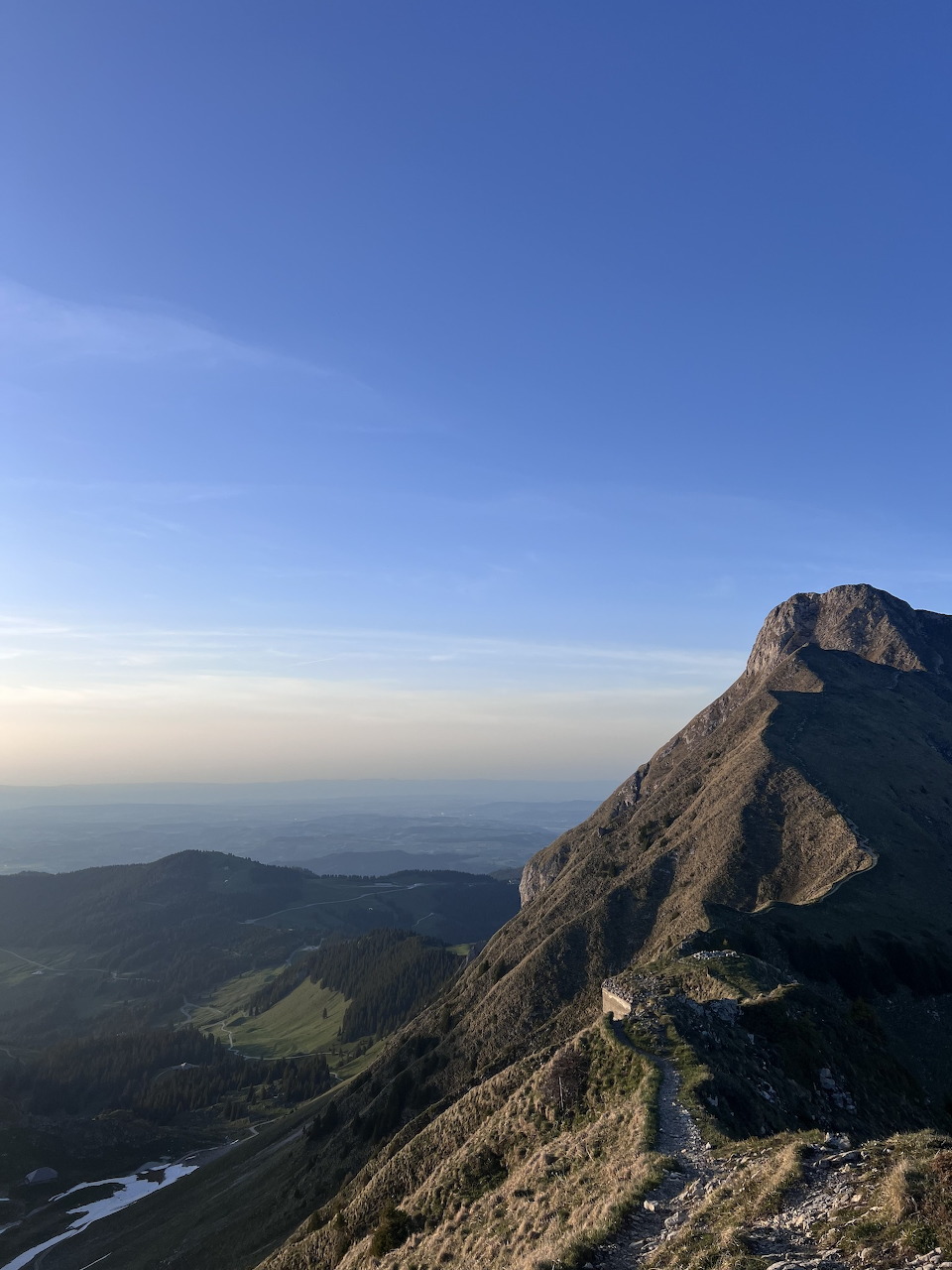 Rocky mountain ridge with steep slopes, green valleys, and a clear blue sky viewed from a high summit