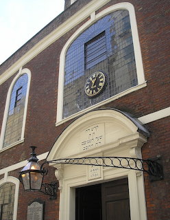 Brick facade of Bevis Marks Synagogue with arched doorway, clock, and iron lantern