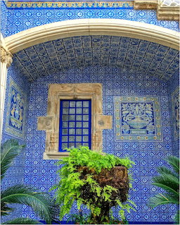 Historic building facade covered in blue and white Portuguese azulejo tiles with arched niche and fern planter