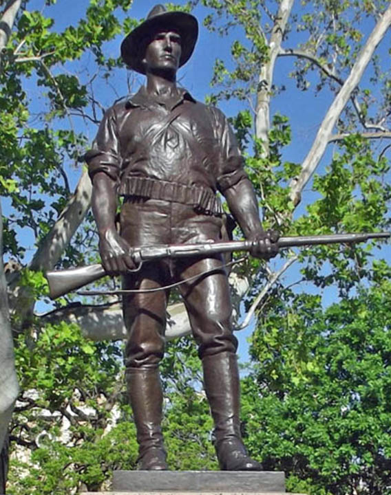 Bronze statue of a uniformed soldier holding a rifle among leafy trees.