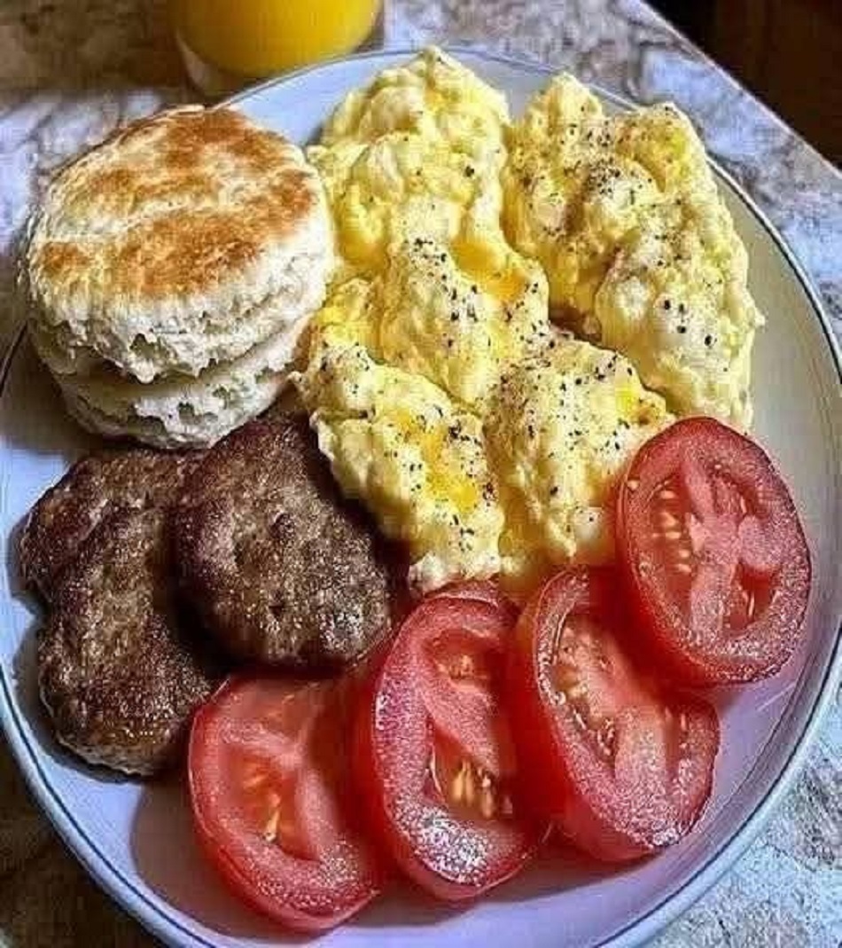 Breakfast plate with eggs, sausage, biscuit, tomatoes, and orange juice