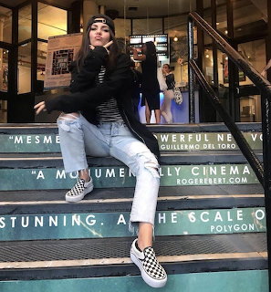 Woman in black top and jeans sitting on teal cinema steps, smiling