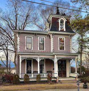 Pink Victorian house with white trim, front porch, and bare trees