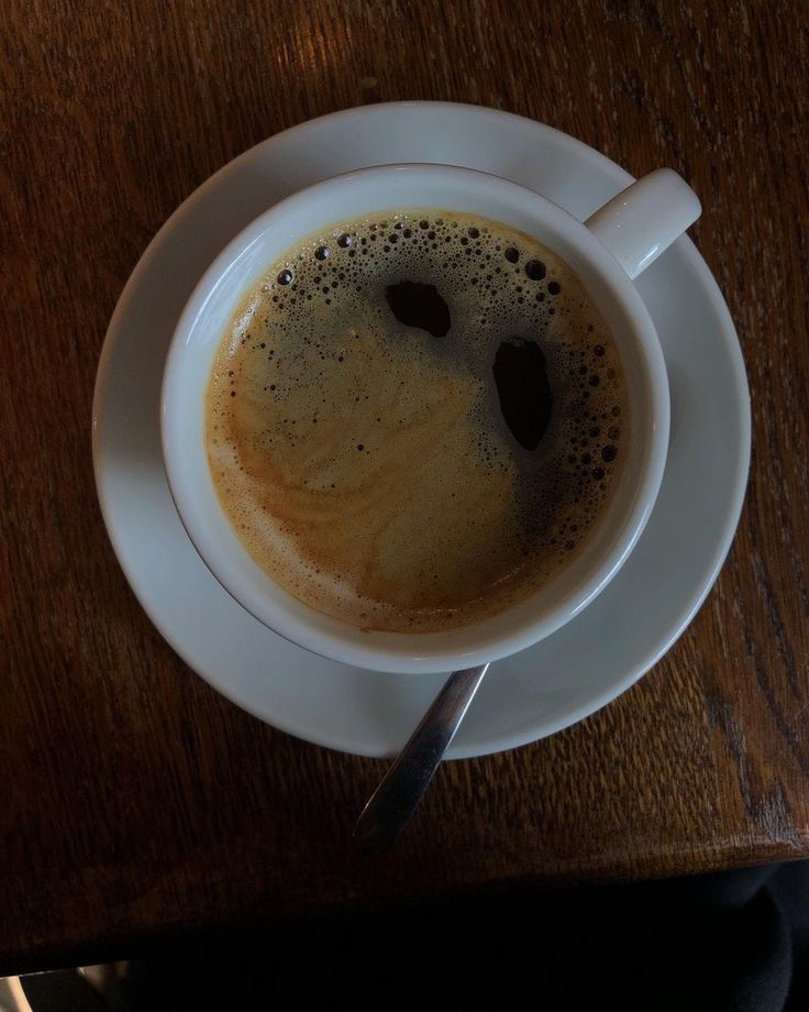 Top-down view of a black coffee in a white cup and saucer with a spoon on a wooden table