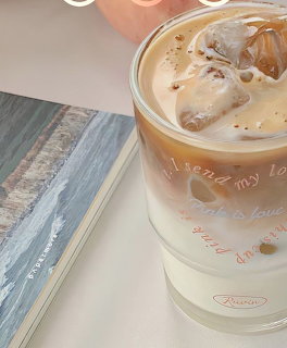 Glass of iced coffee with ice cubes beside a book on a tabletop