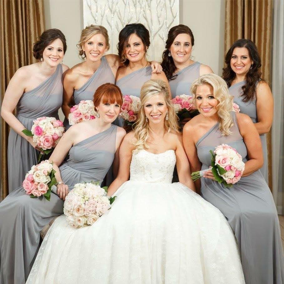 Bride in white wedding dress surrounded by seven bridesmaids in gray dresses holding bouquets