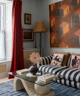 Eclectic living room with striped sofa, red curtain, glass coffee table, and cubist wall art