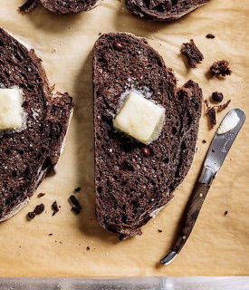 Slices of dark chocolate bread with butter pats on parchment paper next to a butter knife