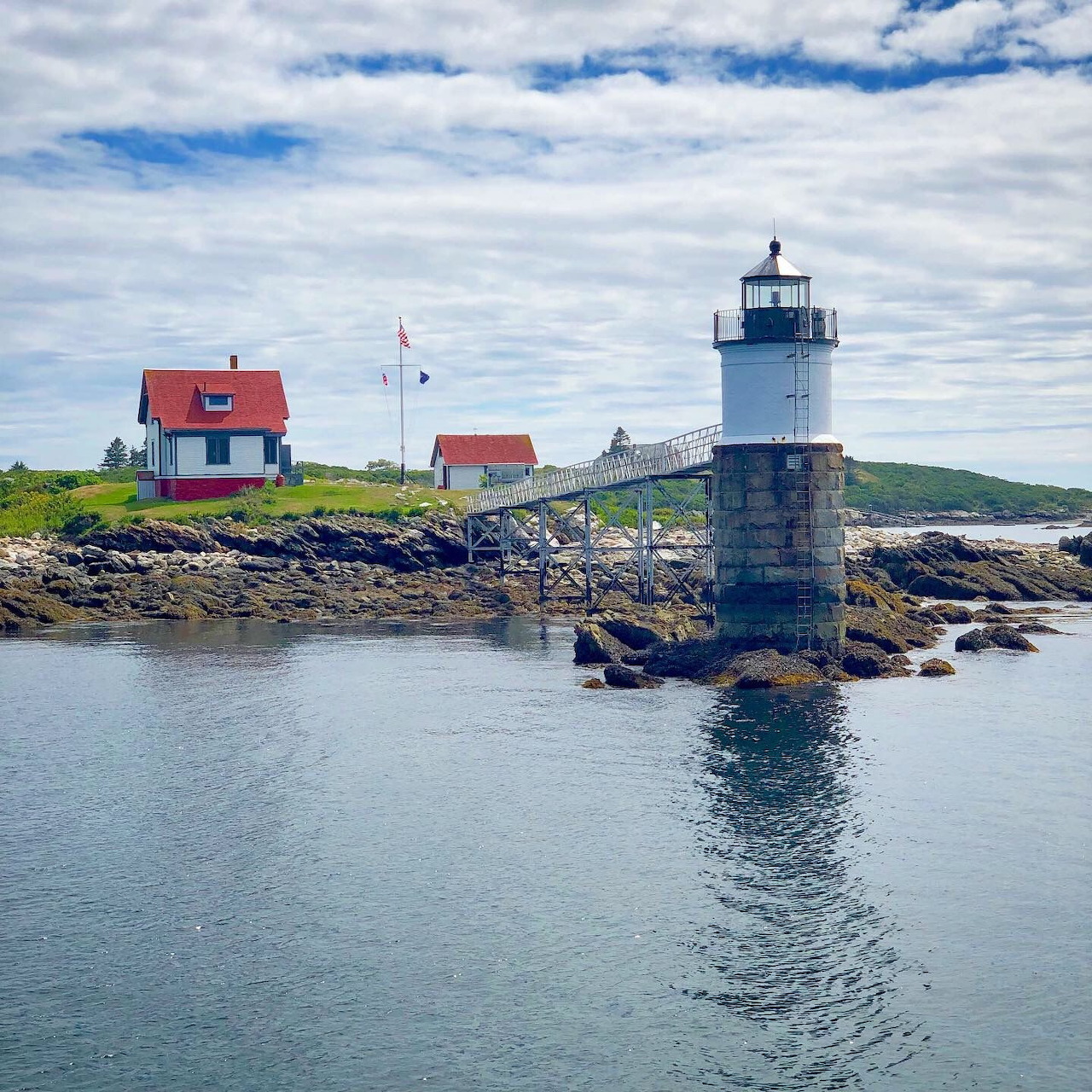 White lighthouse on rocky coast with red buildings under cloudy sky