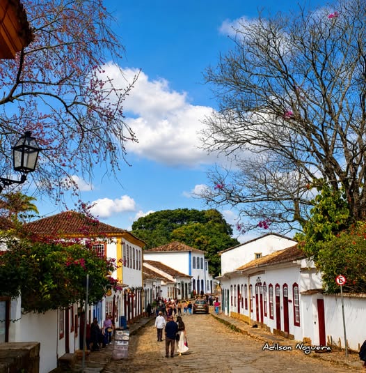 Cobblestone street with white colonial buildings and trees under blue sky in Tiradentes