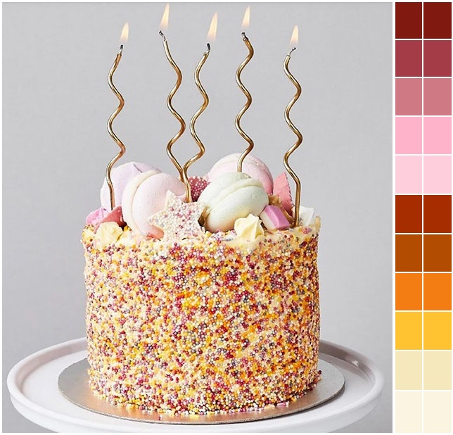 Birthday cake with sprinkles, meringues, and gold candles on white cake stand