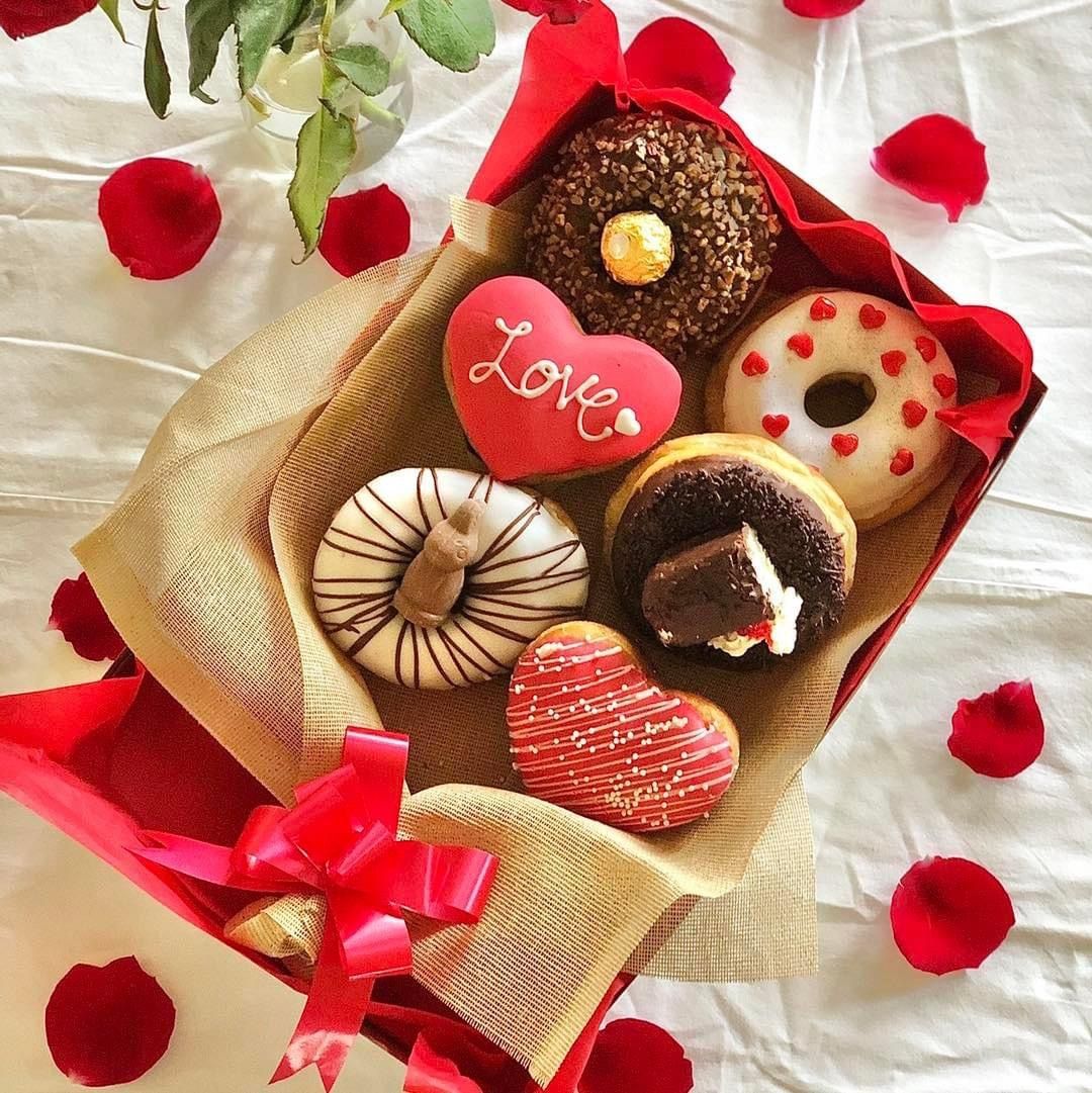 Assorted decorated donuts in gift box with Valentine heart cookie and rose petals