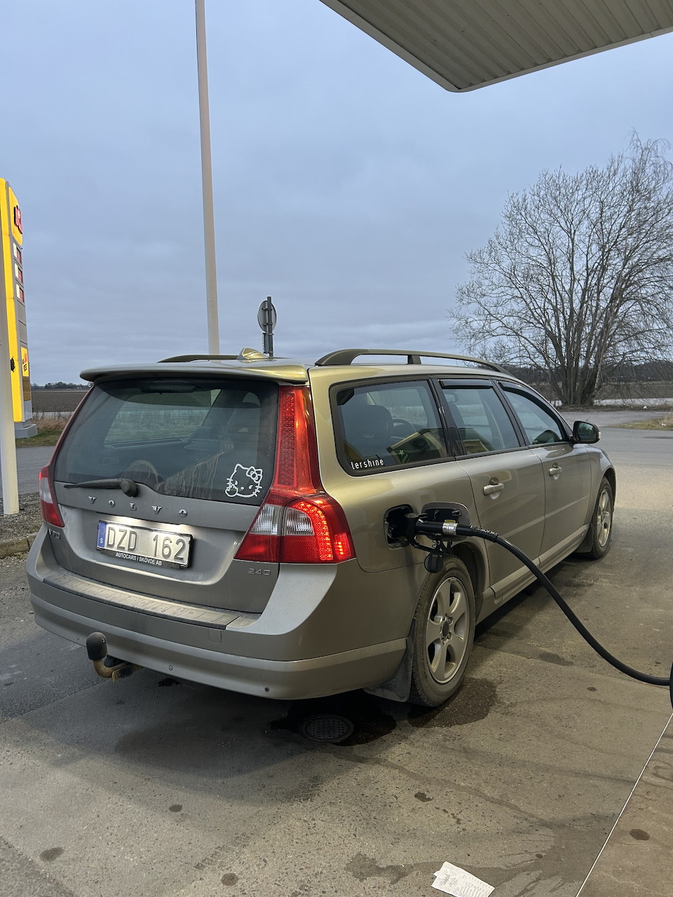 Rear view of a gold Volvo V70 estate car refueling at a gas station on an overcast day