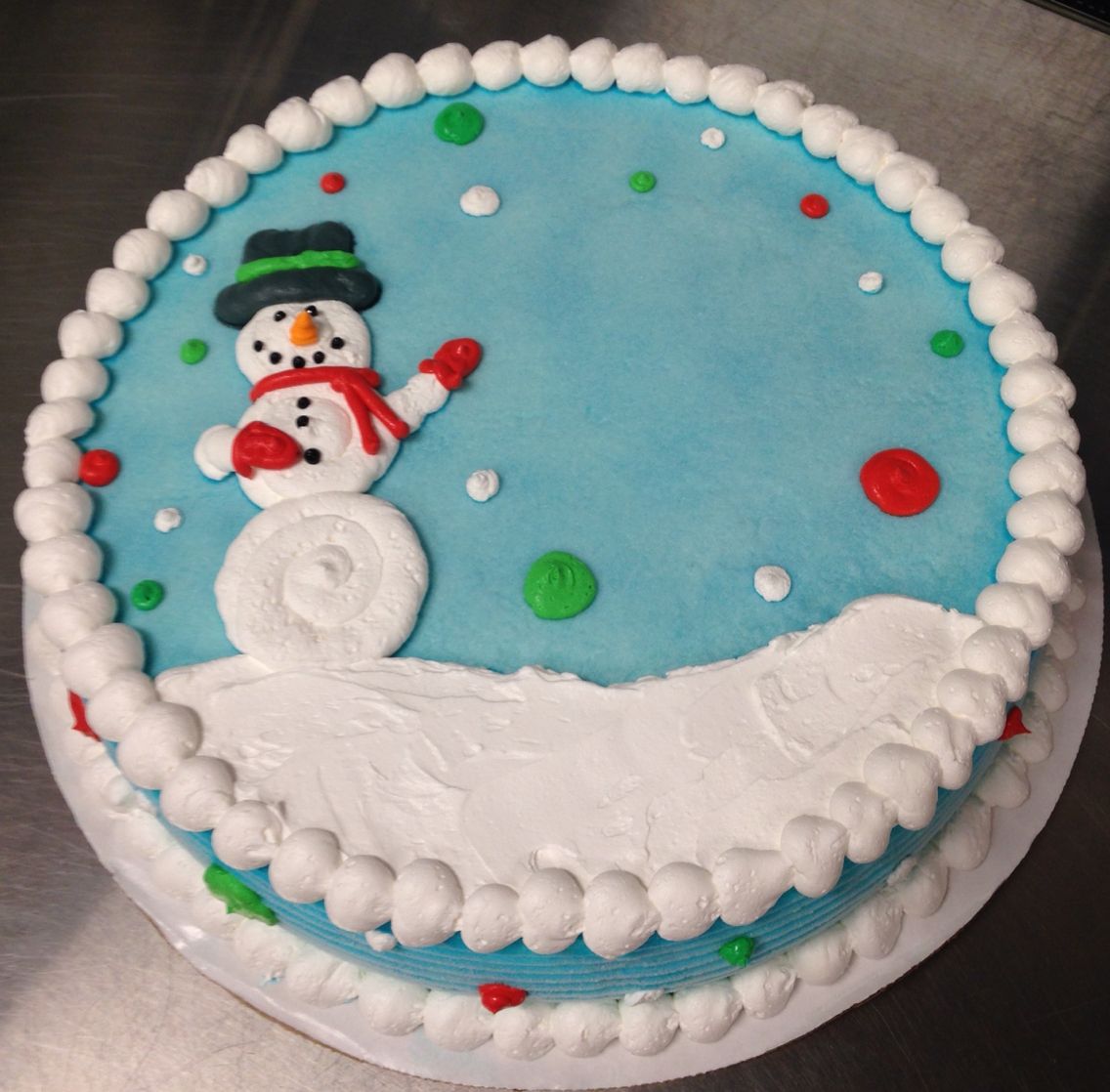 Christmas cake with snowman decoration on blue frosting with white piped border and colorful candy dots