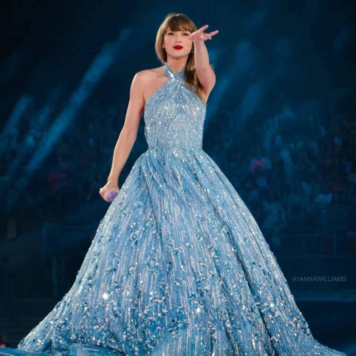 Taylor Swift in glittering blue gown performing on stage with microphone