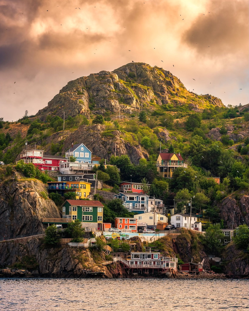 Colorful hillside houses in the Battery, Newfoundland, below a rocky hill and dramatic sky