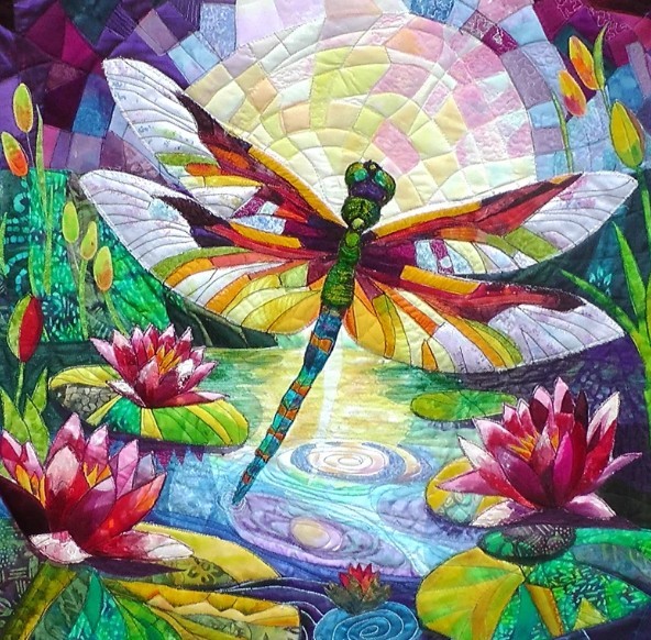 Colorful quilted textile art of a dragonfly with rainbow wings above pink water lilies and reflective water