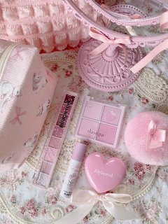 Pink makeup products arranged on floral lace fabric with cosmetic bag and mirror