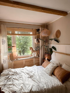 Cozy boho bedroom with unmade bed, plants, and a cat by a sunlit window