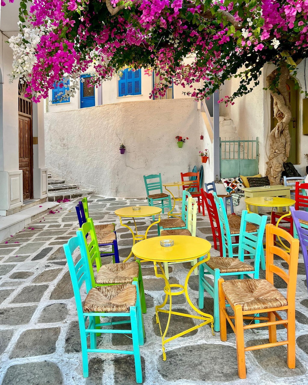 Colorful chairs and tables in a Greek café courtyard with pink bougainvillea overhead, Ios island