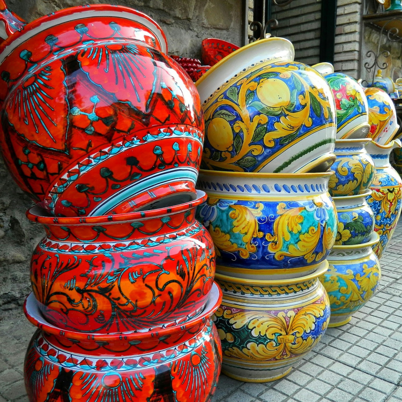 Decorative ceramic vases with vibrant floral designs stacked on a street