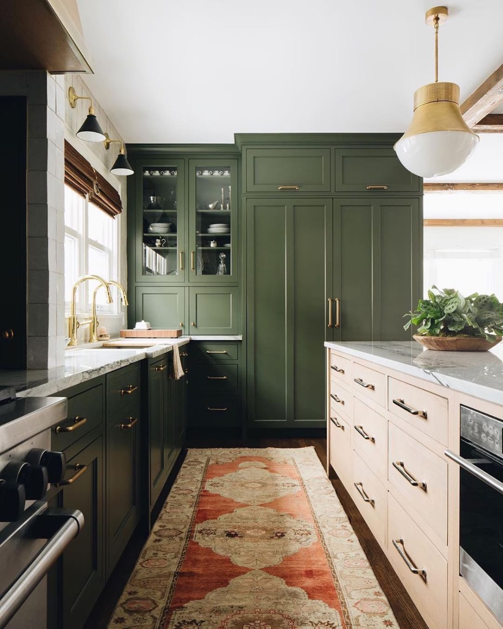 Green and white kitchen with tall cabinets, white counters, brass faucet, and patterned runner rug
