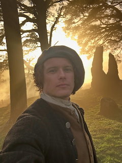 Young man in period clothing and beret standing in a misty sunlit woodland