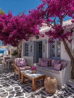 White Greek courtyard with pink bougainvillea trees and outdoor seating with purple cushions