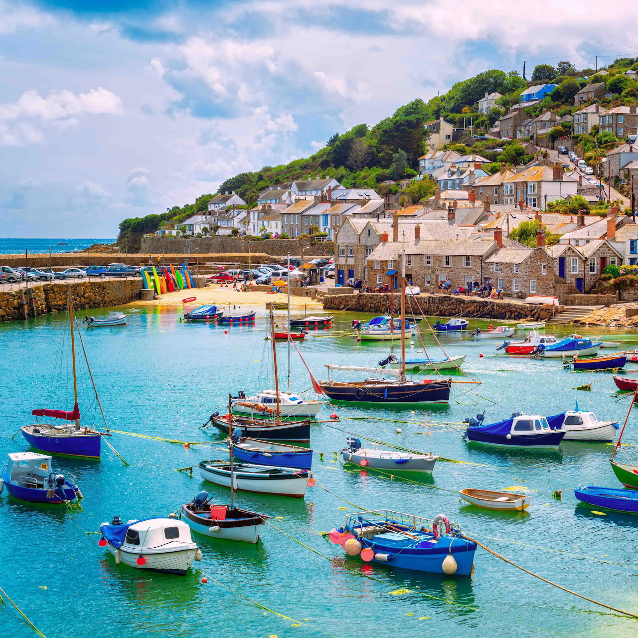 Colorful boats in Mousehole harbour with stone cottages on hillside under blue sky