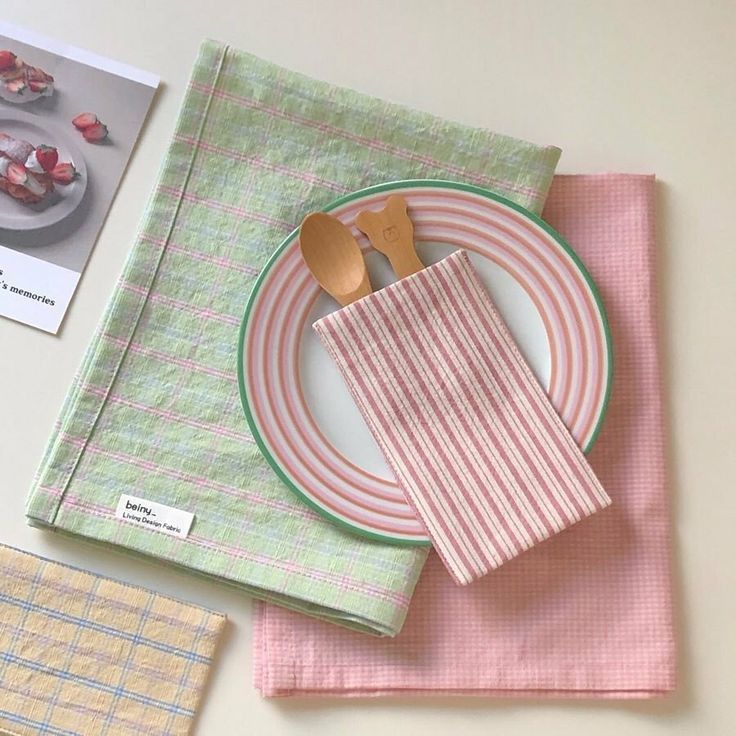 Flat lay of pastel plates, a wooden spoon, striped napkin, and folded fabric placemats