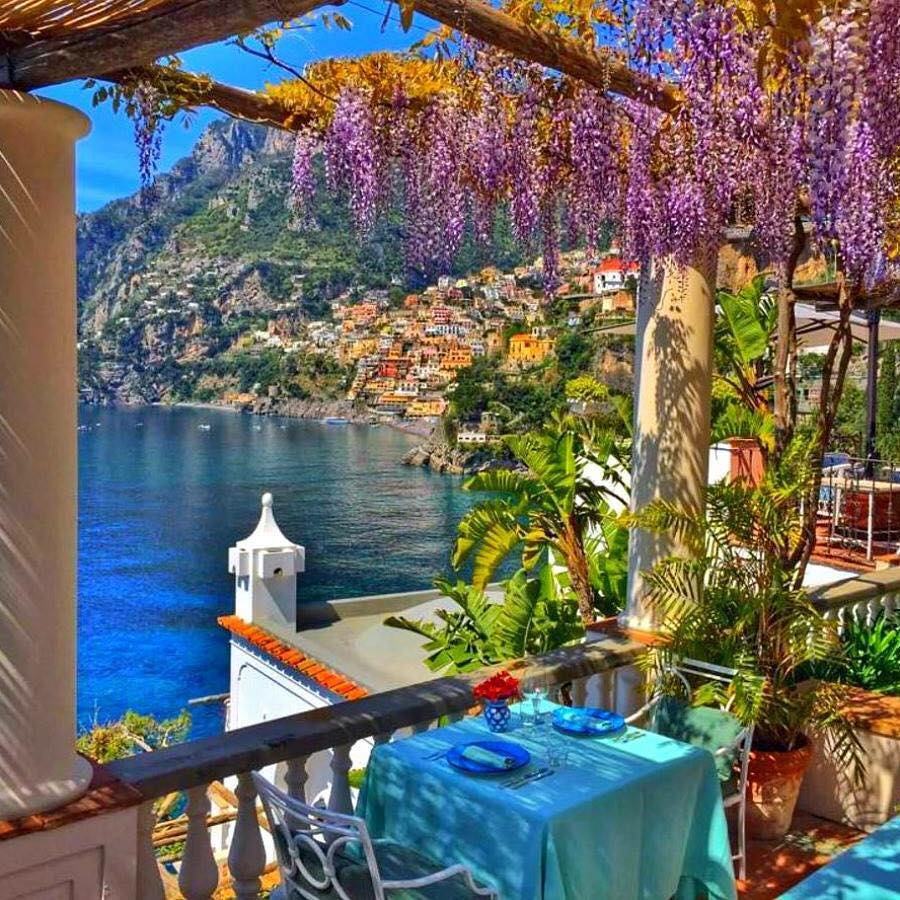 Flower-covered terrace with sea view and cliffside Positano buildings in Italy
