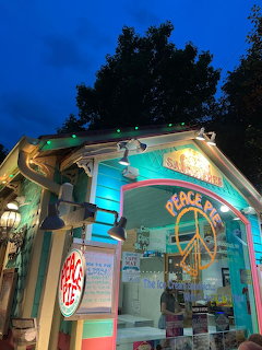 Colorful Peace Pie storefront at dusk with pastel trim and glowing signs beneath a dark blue sky