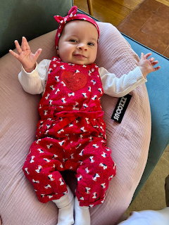 Smiling baby on a pink cushion wearing a red romper and matching headband