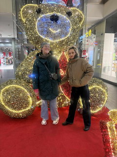 Two women standing in front of a giant golden light-up teddy bear decoration at a shopping center