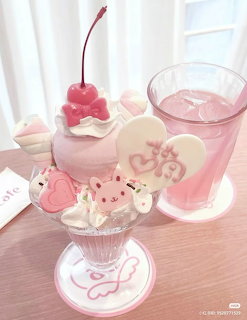 Pink layered dessert in glass with whipped cream, macarons, beverage and decorative cherry on white surface