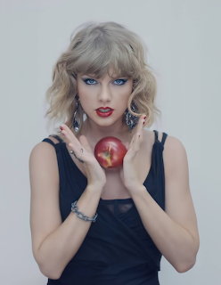 Blonde woman in black top holding a red apple with red lipstick and blue eyes