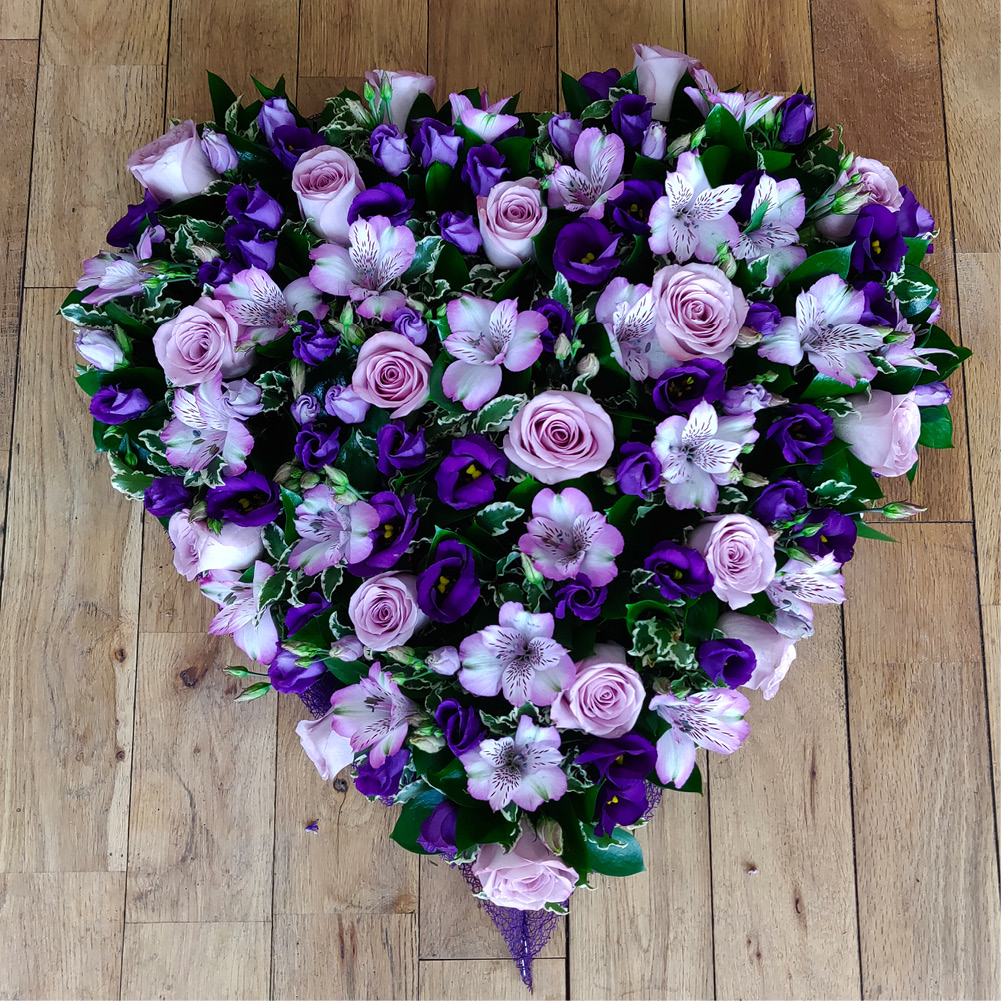 Heart-shaped arrangement of purple roses and flowers on wooden floor