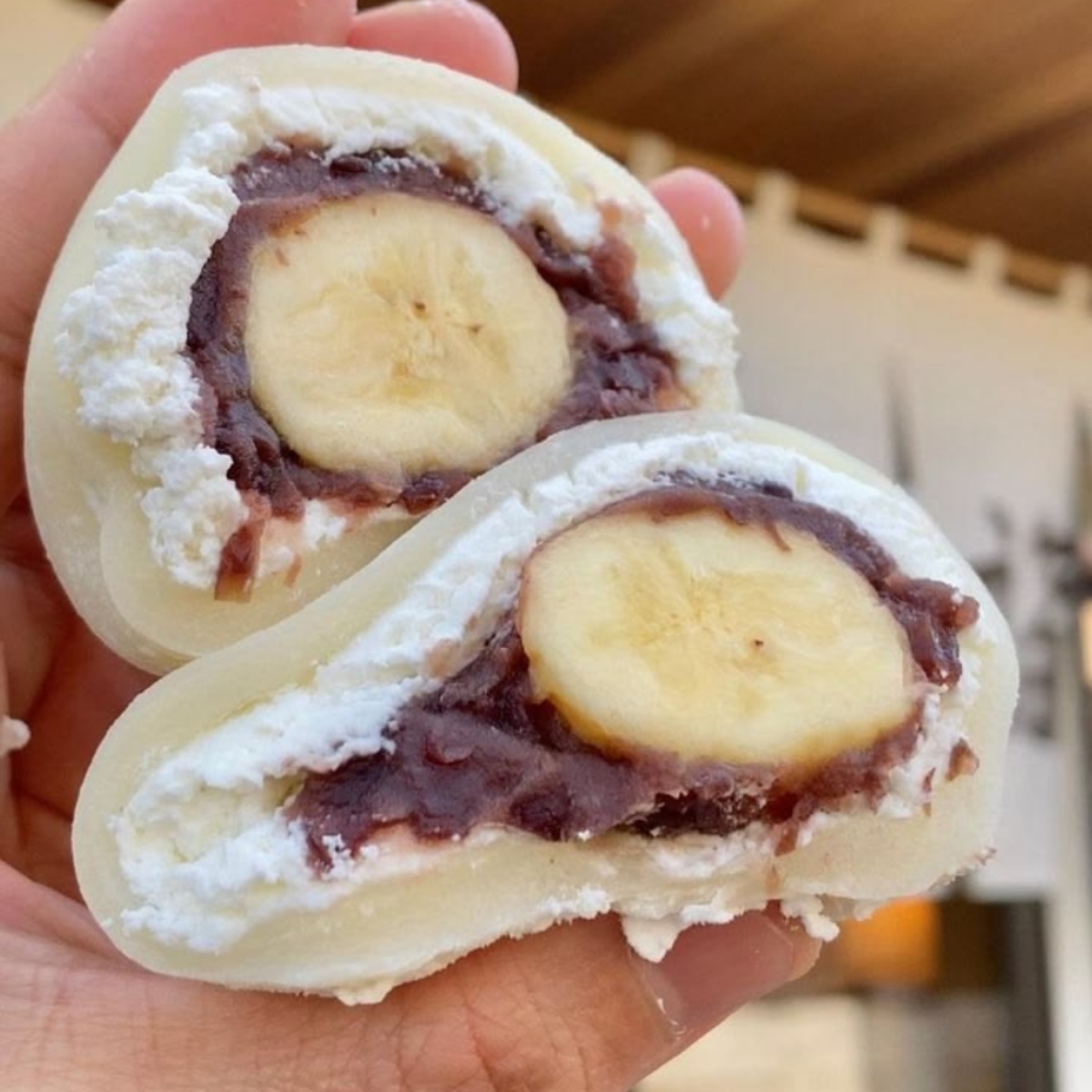 Hand holding two halves of banana daifuku mochi showing banana slices and red bean paste filling inside white mochi
