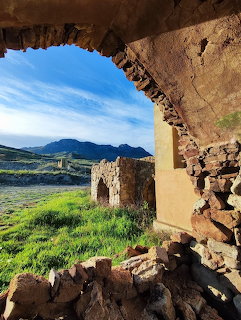 Stone archway of ruined building framing view of green valley and mountains