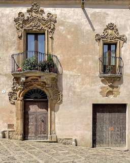 Historic baroque building facade with ornate carved stone doorway, iron balconies, and weathered walls