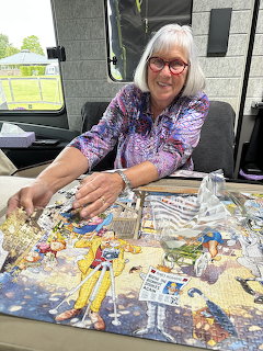 Smiling woman with silver hair assembling a colorful jigsaw puzzle inside a camper van