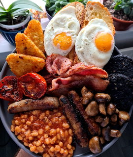 Full English breakfast plate with fried eggs, bacon, sausages, beans, mushrooms, and grilled tomatoes
