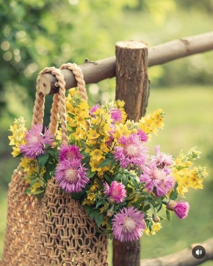 Pink and yellow flowers in a woven bag hanging on a wooden fence outdoors