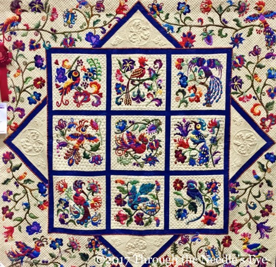Colorful quilt with embroidered birds and floral blocks in a blue bordered patchwork design
