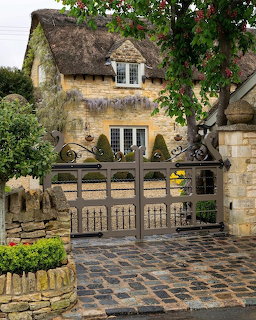 Traditional thatched cottage with stone walls, wooden gate, and rose garden in English countryside