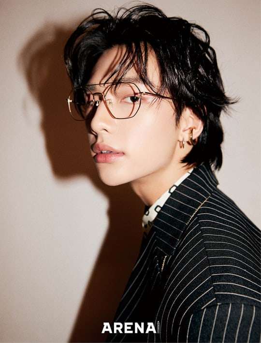 Side profile portrait of young man wearing glasses and striped blazer against beige wall