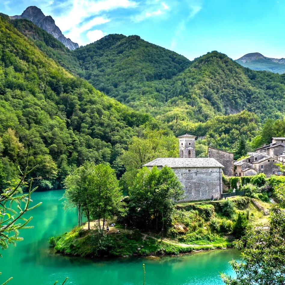 Stone church and village beside a turquoise lake with forested mountains in the background