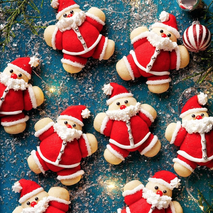 Santa Claus cookies on a blue holiday background with ornaments and greenery